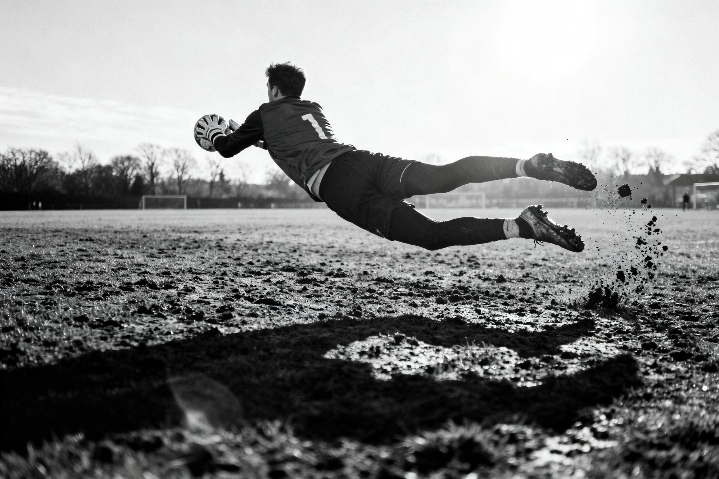 Zwart-wit foto van een keeper horizontaal in de lucht tijdens een redding op een modderig veld